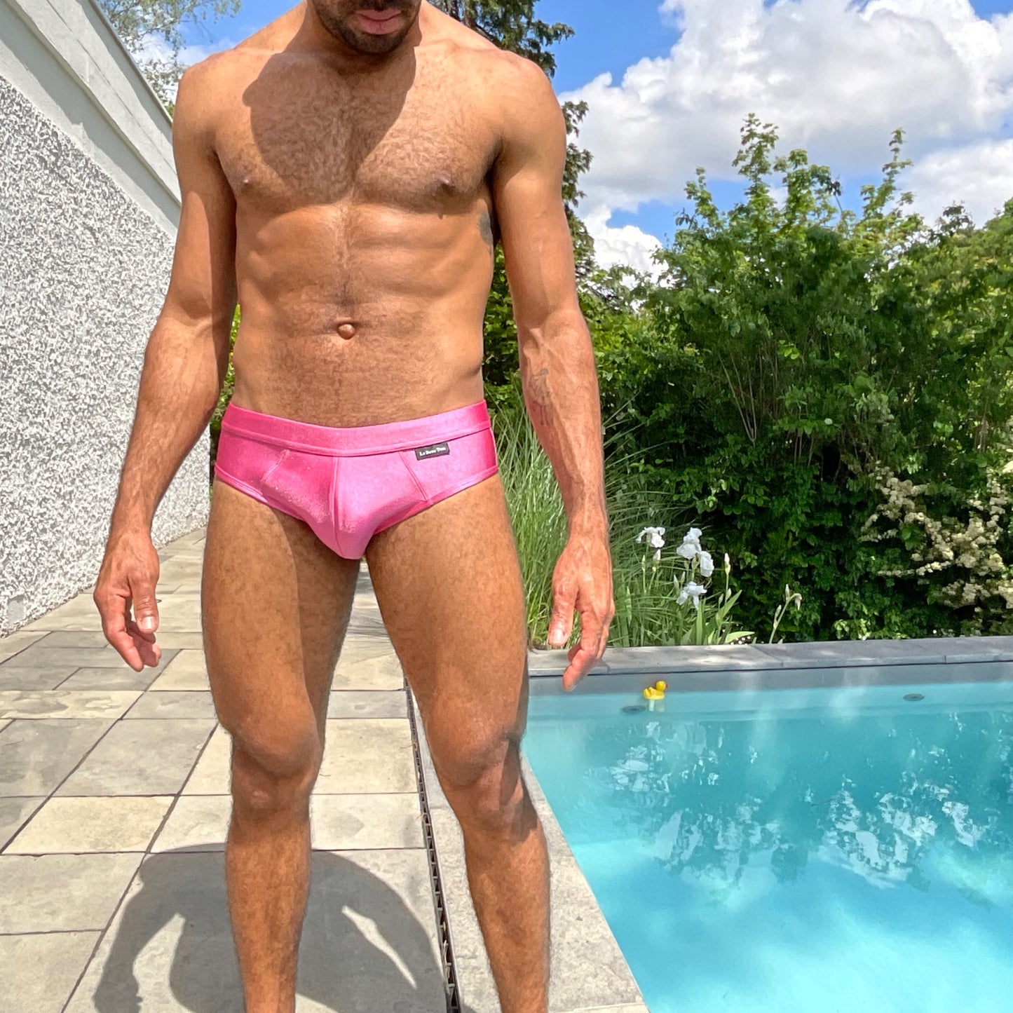 Photo plein pied d'un homme sexy portant le maillot de bain fuschia de la marque gay Française Le Beau Tom. La marque fabrique ce maillot de bain au Portugal.